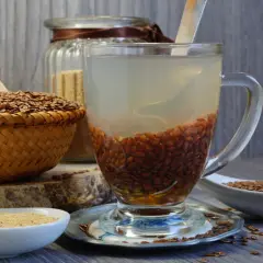 Szklanka z wodą i nasionami lnu, obok koszyk z siemieniem lnianym i miseczka z mąką lnianą. Naturalny kisiel z siemienia lnianego w przygotowaniu.