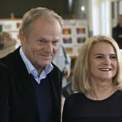 Donald Tusk z żoną, uśmiechnięci, w tle wyborcze plakaty.