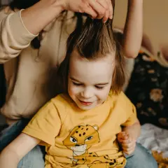 Mama delikatnie rozczesuje kołtuny u dziecka, które uśmiecha się, patrząc w dół.