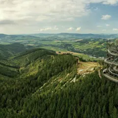 Widok na malowniczy krajobraz z lasami i wzgórzami w Czechach, z dominującą spiralną wieżą widokową.