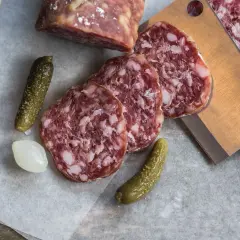 Plasterki salami z widocznym tłuszczem, ogórki konserwowe i cebulka. Salami jest z mięsa wieprzowego i wołowego.