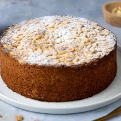 Torta rustica con farina di mandorle, cosparsa di zucchero a velo e pinoli tostati. Un dolce invitante, perfetto per ogni occasione.