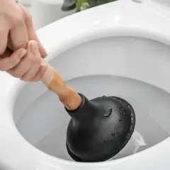 Main d'une personne utilisant une ventouse pour déboucher un WC.