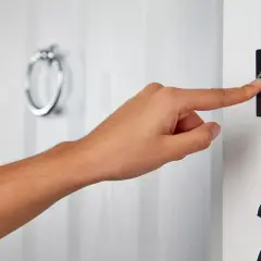 Dłoń naciska fajny dzwonek do drzwi. Obok widoczny numer 28.