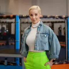Kobieta w dżinsowej kurtce i neonowych spodniach stoi przed klatką MMA. Ile lat ma Aniela Bogusz?