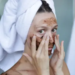Kobieta z ręcznikiem na głowie nakłada na twarz domowy peeling złuszczający do twarzy.