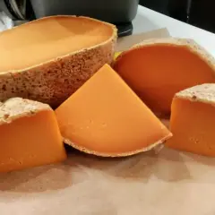 Un queso mimolette peligroso, con su corteza rústica y su vibrante interior anaranjado, se presenta en cuñas y una pieza entera, invitando a una degustación audaz.