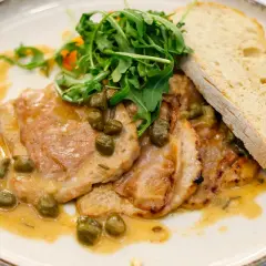 Pyszne saltimbocca alla romana z cielęciną, szynką, szałwią i kaparami w sosie, podane z rukolą i chlebem.