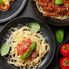 Pyszne spaghetti z sosem pomidorowym i bazylią, posypane czymś, co świetnie sprawdzi się co zamiast parmezanu. Obok talerz z owocami morza i mięsem mielonym.