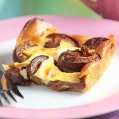 Tranche de clafoutis aux prunes moelleux sur une assiette rose avec une fourchette.