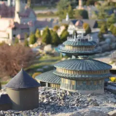 Miniaturowe budowle, w tym okrągły budynek z kopułą i wielopoziomowa konstrukcja, tworzą krajobraz jednego z parków miniatur w Polsce.