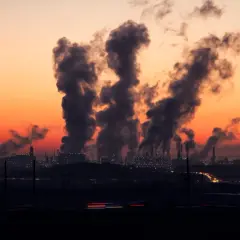 Dymiące kominy fabryk na tle pomarańczowego zachodu słońca.