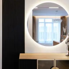 Elegancka aranżacja lustra w przedpokoju z podświetleniem. Na komodzie stoją ozdobne figurki ptaków.