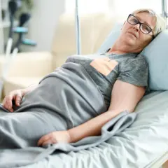 Starsza kobieta leży w łóżku. Jej komfort zapewnia materac przeciwodleżynowy, refundowany przez NFZ.