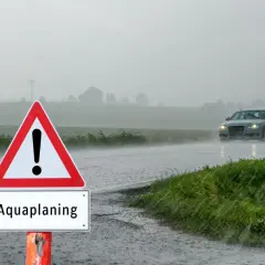 Señal de advertencia de aquaplaning en un día lluvioso. Un coche circula por la carretera mojada. ¿Qué puede hacer para evitar el aquaplaning?