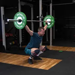 Mężczyzna w pozycji przysiadu z podniesionym sztangą, przygotowuje się do podrzutu. To element dwuboju olimpijskiego.