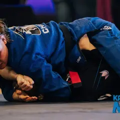 Två kvinnor i blå och svarta gi tävlar i bjj sm. En kämpar sig framåt, fokuserad på att vinna.