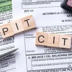 Drewniane klocki z literami PIT i CIT leżą na formularzach podatkowych. Temat: podatek od sprzedaży nieruchomości po upływie 5 lat.