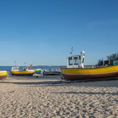 Żółte łodzie rybackie na piaszczystej plaży w Sopocie, spokojne morze i błękitne niebo.