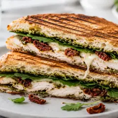 Pyszne panini z kurczakiem, mozzarellą, rukolą i suszonymi pomidorami, z sosem pesto. Idealne na lunch!