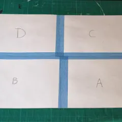 Papier divisé en quatre sections (A, B, C, D) par du ruban adhésif bleu rayé, prêt à créer un motif.