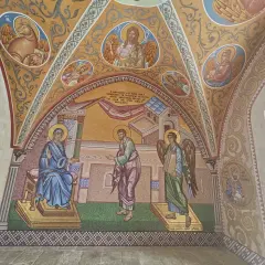Mozaika przedstawia scenę biblijną z postaciami w stylu sztuki sakralnej. Widać Matkę Boską, anioła i mężczyznę, a także symbole religijne.