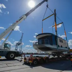 Dźwig podnosi łódź mieszkalną, która jest przewożona ładunkiem gabarytowym. Tylko specjalistyczny transport pozwala na takie operacje.