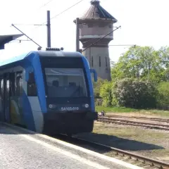 Niebieski pociąg SA103-010 czeka na pasażerów na peronie. W tle stara wieża ciśnień i drzewa. Wygodny wicie dojazd PKP.