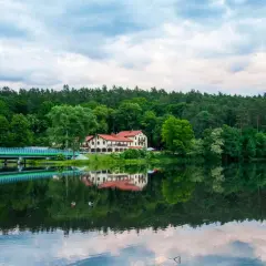 Malowniczy hotel nad jeziorem, z mostem i lasem w tle. Idealne miejsce na rodzinne wakacje, oferujące atrakcje dla dzieci.