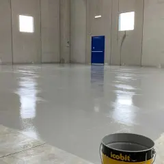 Pavimento in resina epossidica appena posato, lucido e riflettente. Un secchio di prodotto è visibile in primo piano, pronto per risolvere eventuali problemi di applicazione.