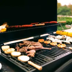 Viande, crevettes, huîtres et maïs grillés sur un barbecue gaz ou charbon. Des saucisses enroulées cuisent sur la grille supérieure.