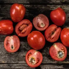 Röda tomater, hela och halverade, ligger på en mörk träyta. Vissa visar tecken på fosforbrist tomat, med mörka fläckar i mitten.