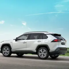 Biały Suzuki Across jedzie po drodze, a jego sylwetka lśni niczym ignis na tle błękitnego nieba.