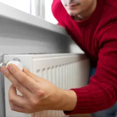 Mężczyzna w czerwonym swetrze reguluje termostat grzejnika, pokazując, jak zaoszczędzić na ogrzewaniu.