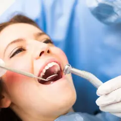 Pacjentka u dentysty, który bada jej dziąsło. Może to być związane z ropniem na dziąśle domowe sposoby.