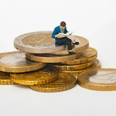 Figurka siedząca na stosie monet euro, czytająca gazetę. Symbolizuje eurocent pożyczki do domu.