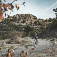 Ciclista en ruta de gravel, disfrutando del paisaje montañoso y el pueblo al fondo. Una aventura de montsec bikepacking loop.