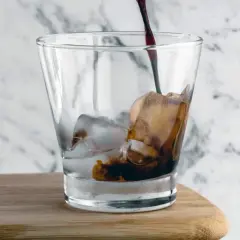 Mörk, rik cold brew kaffe hälls över is i ett glas.