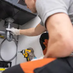 Plombier ajustant une canalisation PVC sous un évier. Outils à portée de main pour le dépannage.