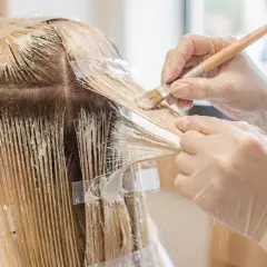 Manos enguantadas aplican tinte para crear mechas blancas en cabello rubio.