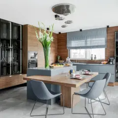 Nowoczesna kuchnia z wyspą, stołem i krzesłami. Oświetlenie pokoju podkreśla eleganckie wnętrze, witryny ze szkłem i drewniane detale.