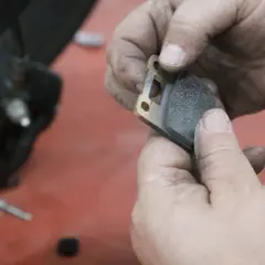 Manos sucias sostienen una pastilla de freno de moto lista para el cambio.