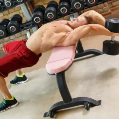 Mężczyzna wykonuje ćwiczenia na klatkę piersiową z hantlem na ławce skośnej.