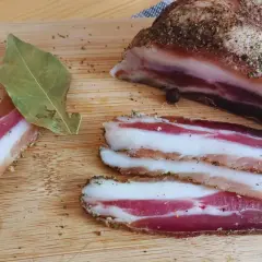Pancetta co to? Pokrojony w plastry, przyprawiony boczek na desce. Obok liść laurowy i kawałek większego kawałka.