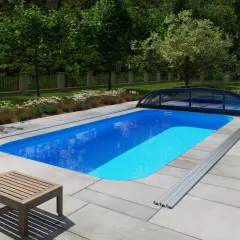 Niebieski basen ogrodowy z pokrywą, otoczony płytkami, meblami i zielenią.