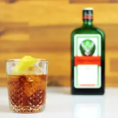 Szklanka z drinkiem i plasterkiem cytryny, obok butelka Jägermeister. Idealny na wieczór z przyjaciółmi, z nutą jagermeister orange.