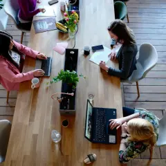 Kobiety pracują przy drewnianym stole, jedna z nich zastanawia się, czy działalność gospodarcza wlicza się do stażu pracy.