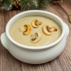 Crema de champiñones servida en un cuenco blanco, decorada con rodajas de champiñones salteados. Una cuchara dorada descansa a la derecha.