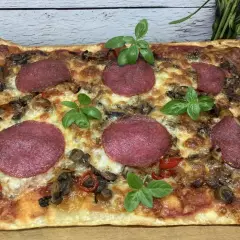 Prostokątna pizza z salami, pieczarkami i papryką, ozdobiona listkami bazylii. Idealne dodatki dla miłośników klasyki.
