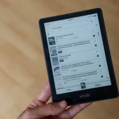 Main d'une personne tenant un livre format Kindle affichant une liste de titres, dont "Becoming a Supple Leopard" et "The Lean Startup".